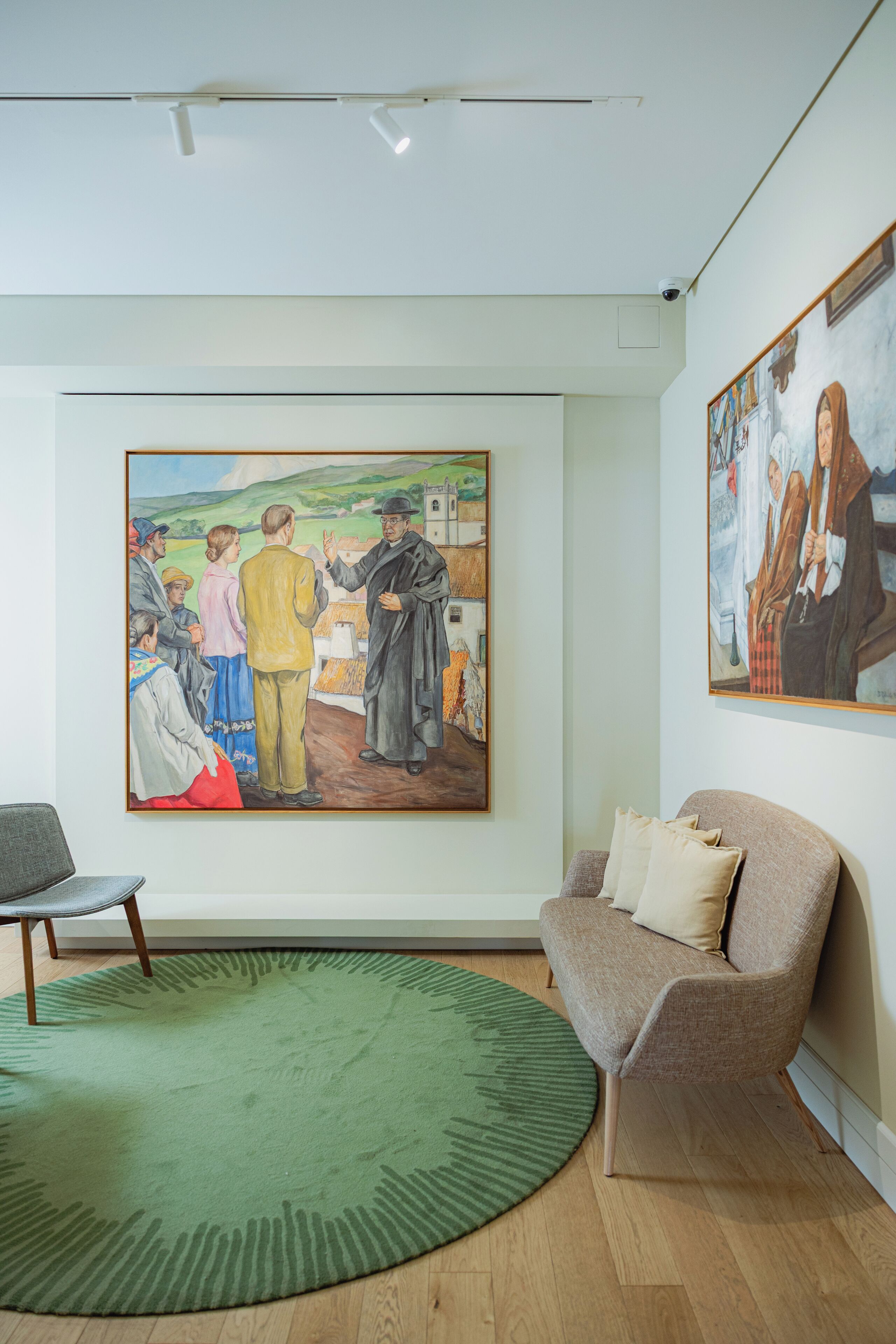 A room with a large painting on the wall, a green rug, a brown sofa, and a small table.