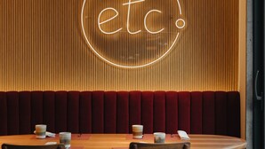 A restaurant interior with a wooden table, red upholstered booth seating, and a neon sign reading "etc.".