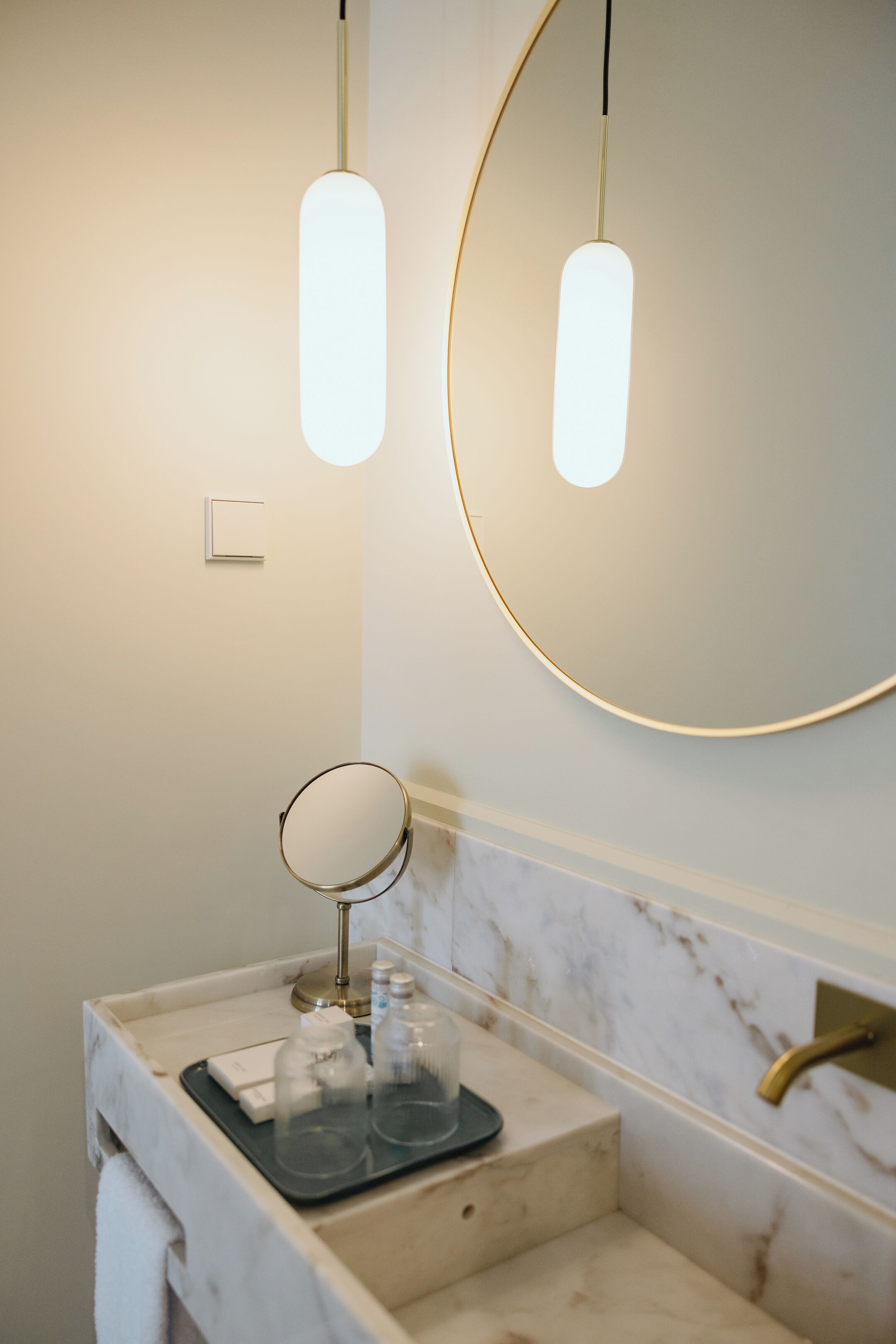Une salle de bain avec un lavabo en marbre, un miroir rond et deux lampes suspendues.