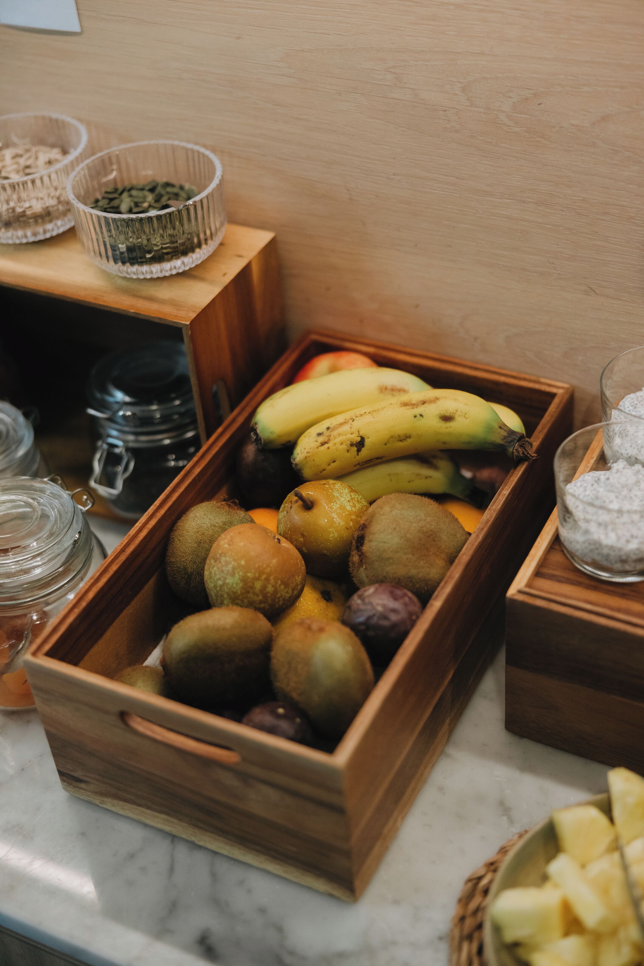 A wooden fruit and nut tray on a marble countertop.