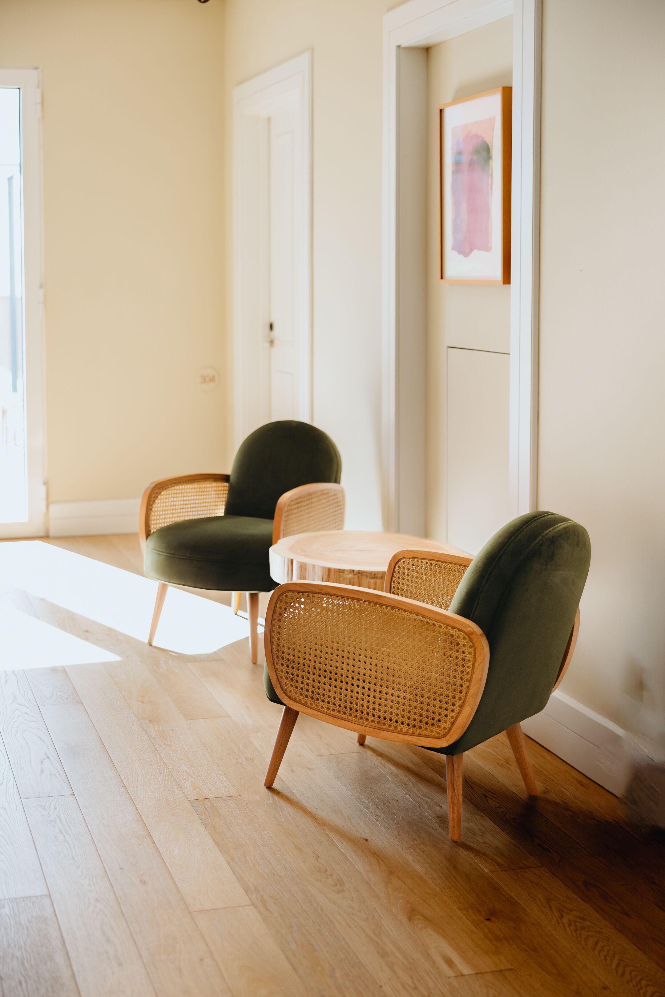 Une pièce avec un plancher en bois, un fauteuil recouvert d’un tissu vert, un fauteuil en osier et une petite table ronde.