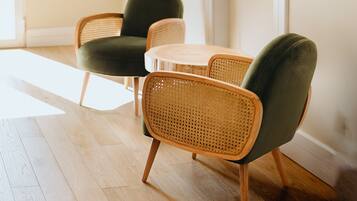 A room with a wooden floor, a green upholstered chair, a wicker chair, and a small round table.