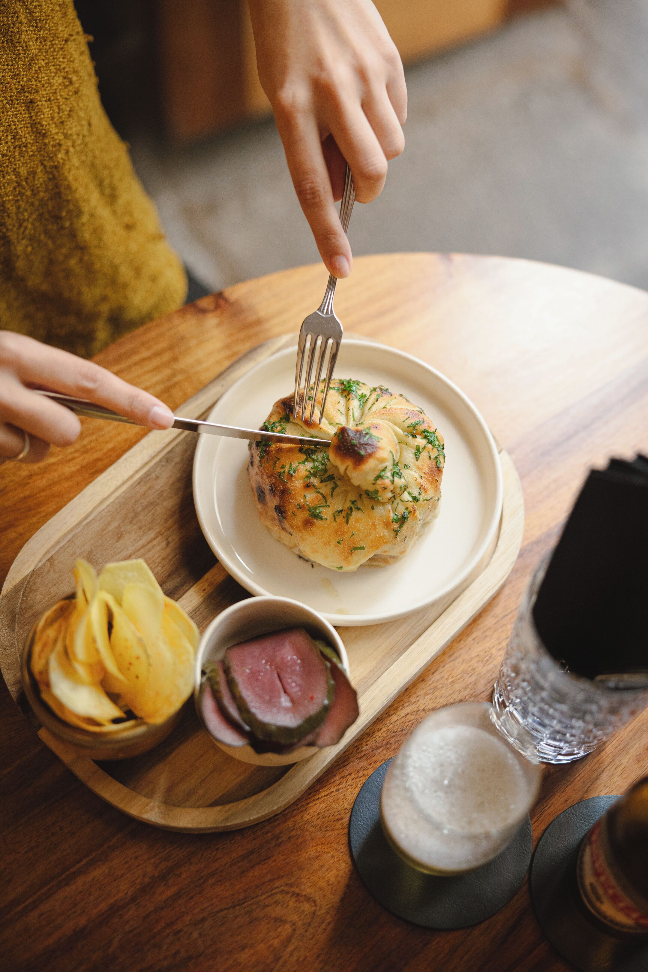 Une table à manger avec une assiette de nourriture, une fourchette, un verre de bière et un petit bol de chips.