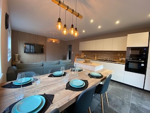 Enjoy meals in this stylish dining area with a table for four, flat-screen TV, and modern kitchen in the background.
