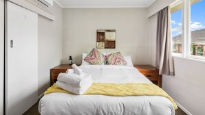 Una camera d'albergo con un letto, un comodino, un condizionatore d'aria, una finestra con tende e vista esterna.