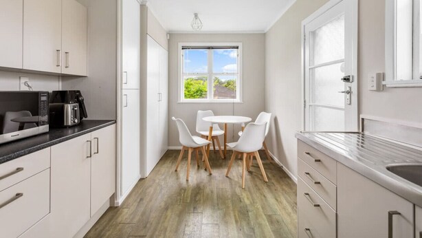 Una cucina moderna con mobili bianchi, un piano di lavoro nero e un'area pranzo con sedie bianche e un tavolino rotondo.