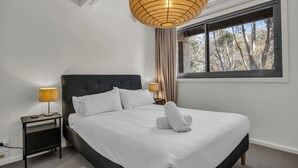 A neatly made bed with white linens, two bedside lamps, a dark headboard, and a large window with curtains. - Warrina 8 | Thredbo | Large & on the Village flat (Thredbo)