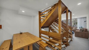 A modern interior with a wooden staircase, a wooden dining table, and a sofa. - Warrina 8 | Thredbo | Large & on the Village flat (Thredbo)
