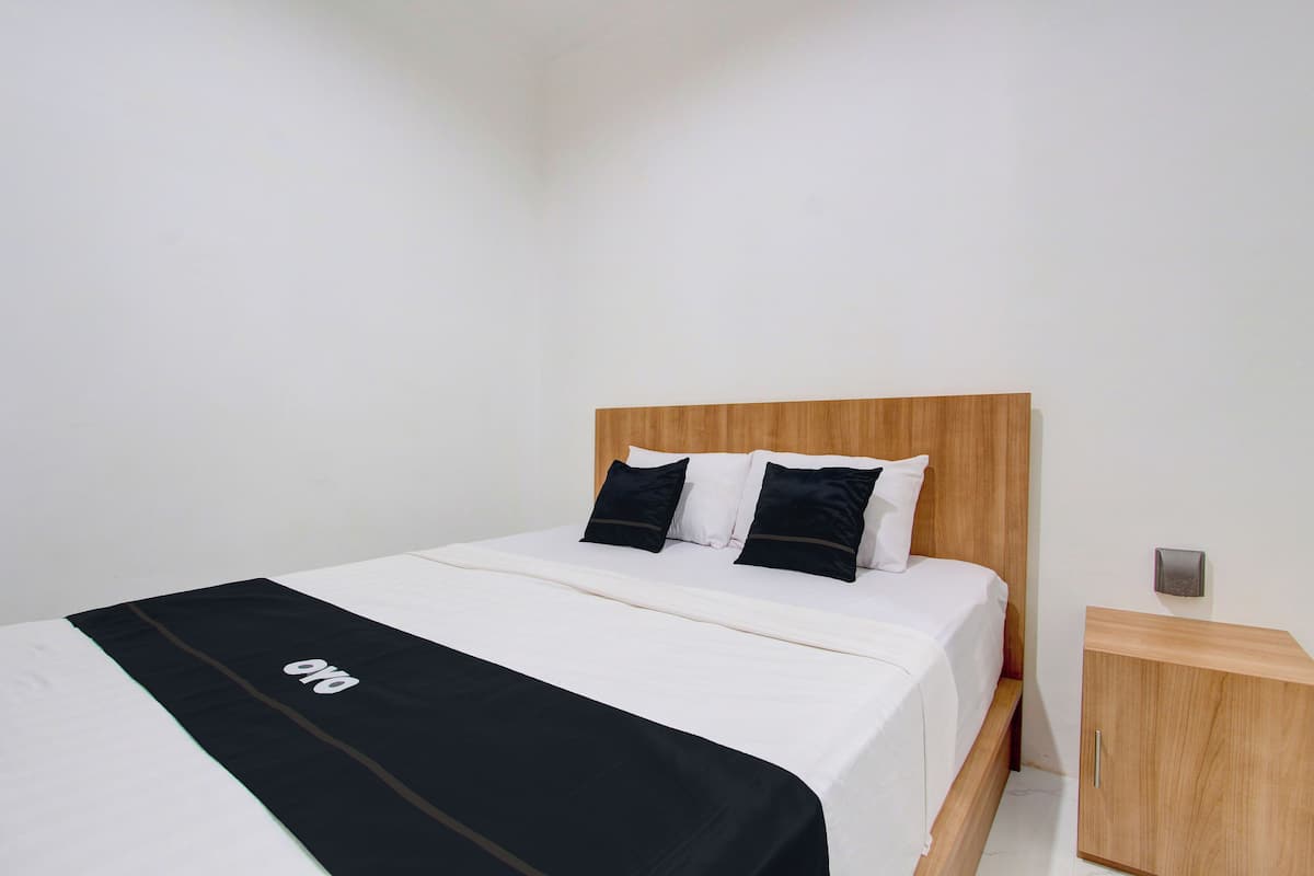 A neatly made bed with a wooden headboard, white bedding, and two black pillows.