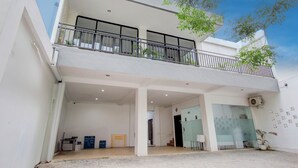 Un edificio de dos pisos con balcón, entrada cubierta y puerta de vidrio que da a una habitación.