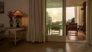 A room with a wooden floor, a table with two vases, a lamp, and a view of a balcony with chairs and a table. - Regarda - "Villa Infinity" with private pool and lake view (Bardolino)