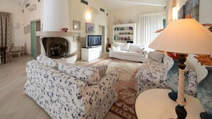 A spacious living room with a fireplace, a television, a white sofa, and a patterned rug. - Regarda - "Villa Infinity" with private pool and lake view (Bardolino)