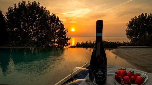 A bottle of Zonin Prosecco on a table with a plate of strawberries and a glass, overlooking a pool at sunset. - Regarda - "Villa Infinity" with private pool and lake view (Bardolino)