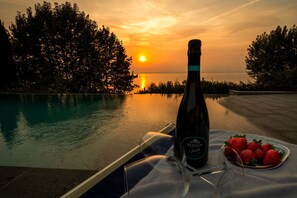 Eine Flasche Zonin Prosecco auf einem Tisch mit Erdbeeren und einem Glas, Blick auf einen Pool bei Sonnenuntergang.