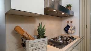 A kitchen with a rustic wooden crate holding biscuits and a pineapple, a gas stove, and a hanging pot holder. - Regarda - "Villa Infinity" with private pool and lake view (Bardolino)
