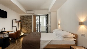 A modern bedroom with a wooden bed, a desk, and a chair. There is a stone wall and a view of the outside. - alle Stelle b&b (Anacapri)