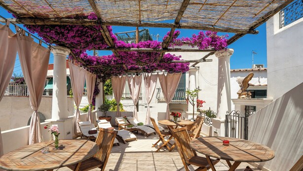 An outdoor patio with wooden furniture, a pergola with purple flowers, and a view of the cityscape. - alle Stelle b&b (Anacapri)
