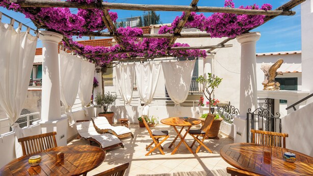 An outdoor patio with wooden furniture, white curtains, and purple flowers. - alle Stelle b&b (Anacapri)