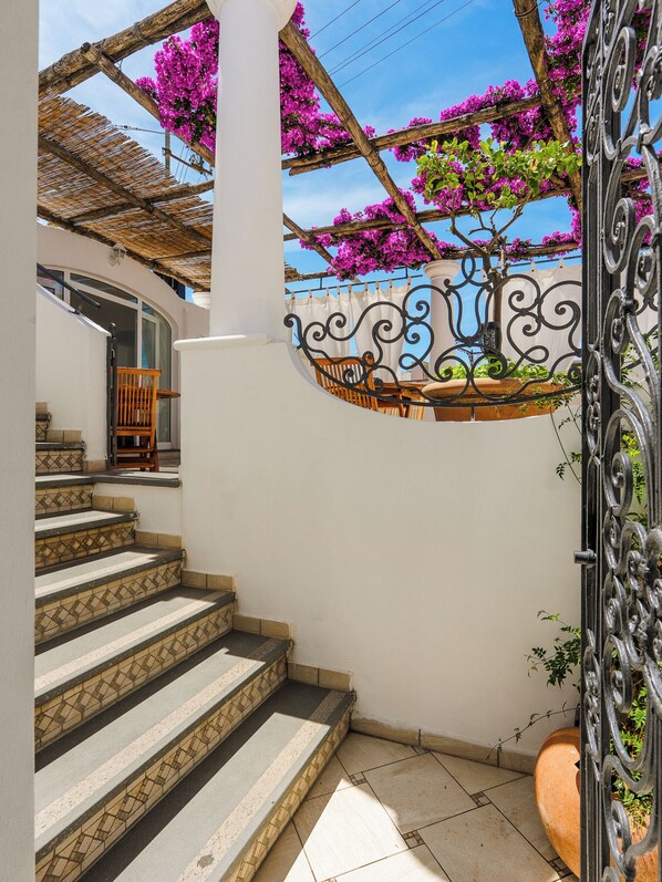 Una escalera con baldosas estampadas, una silla de madera y un portón de hierro forjado.