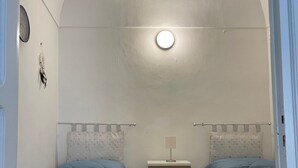 A small, narrow room with two beds, a nightstand, a wall clock, and a ceiling light. - Appartement en Sicile Près de la mer Pour 1-6 Personnes Avec Terrasse et Wifi (Balestrate)