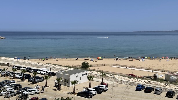 A beachside parking lot with cars and a small building, overlooking a sandy beach with umbrellas and people. - Appartement en Sicile Près de la mer Pour 1-6 Personnes Avec Terrasse et Wifi (Balestrate)