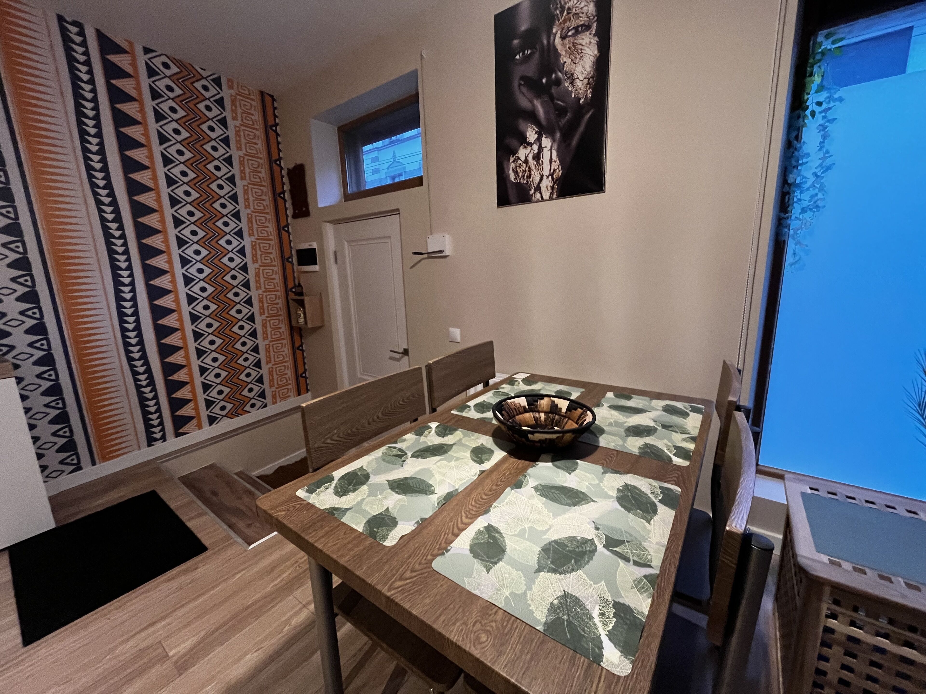 Un coin repas avec une table dressée pour deux personnes, un mur orné d’un motif, une fenêtre et une affiche accrochée au mur.
