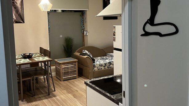 En kompakt opholdsstue med tekøkken, spiseplads og sofa.