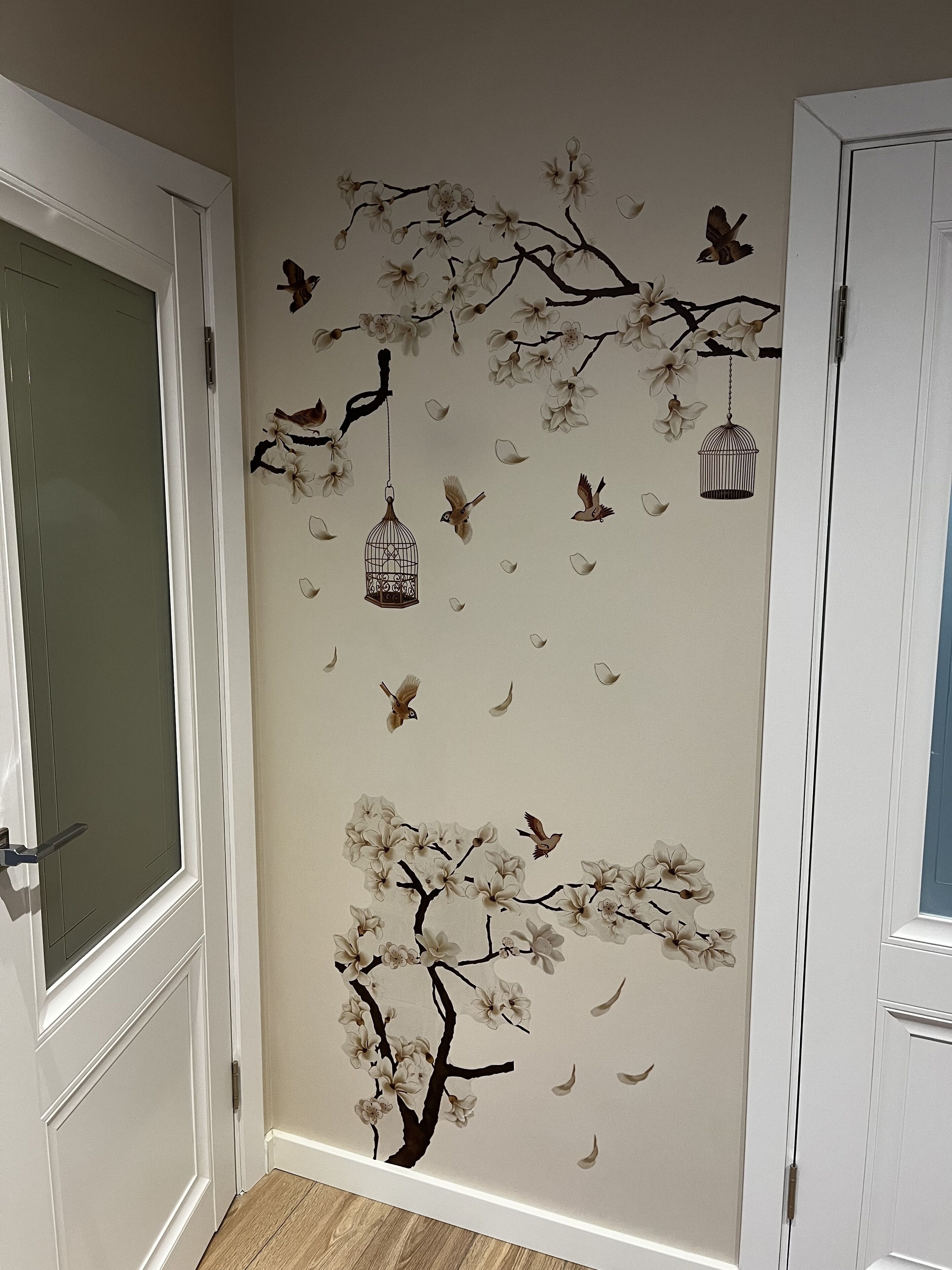 Un couloir orné d’une fresque murale représentant un arbre avec ses branches, des oiseaux et des cages à oiseaux suspendues.