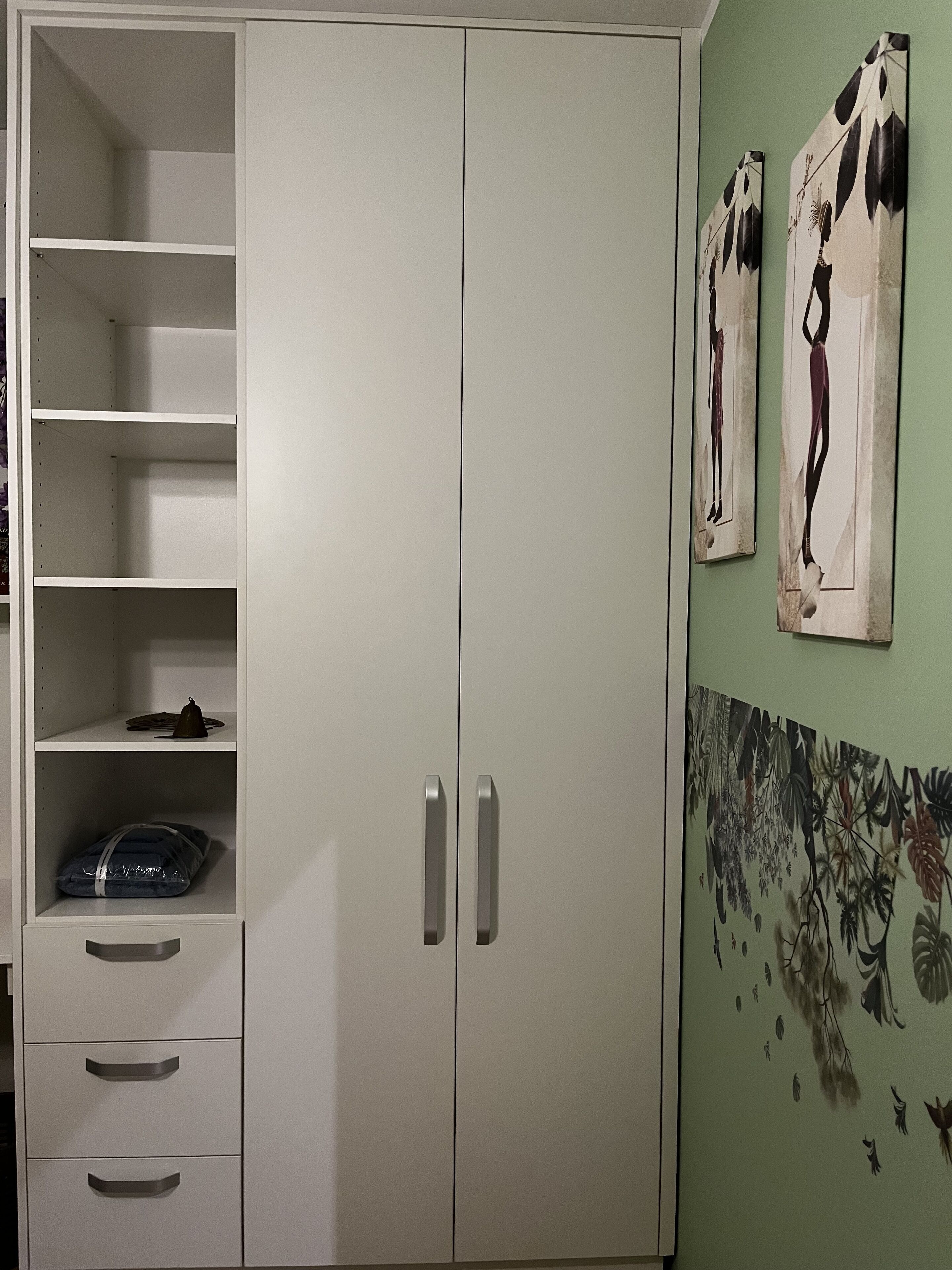 A white wardrobe with multiple shelves and drawers, a mirror, and two wall-mounted artworks.