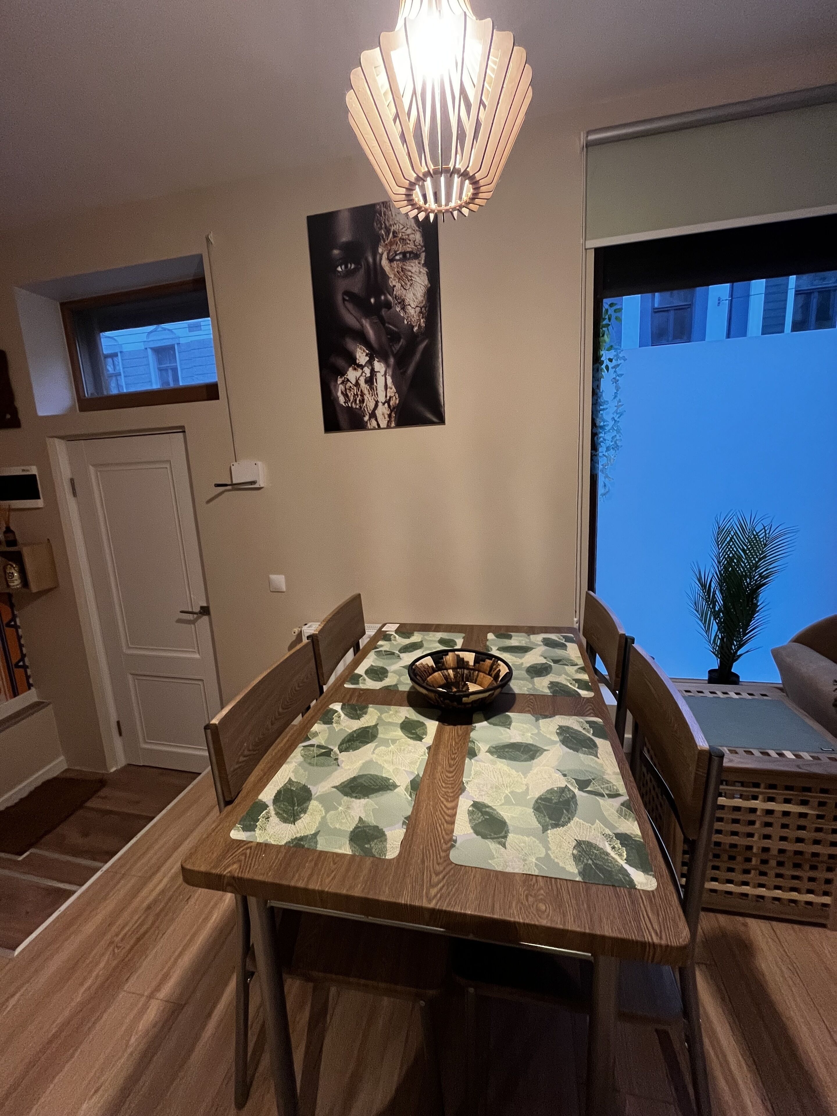 Un espace repas comprenant une table, des chaises, un lustre, une œuvre d’art accrochée au mur et une fenêtre donnant sur un paysage.