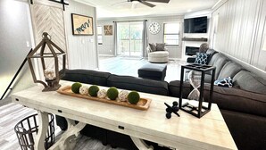 A modern living room with a sofa, a dining table with decorative items, a ceiling fan, and a fireplace. - STAY HERE! 2 Homes sleep up to 28! Private cove 2 docks and personal boat launch (Sevierville)