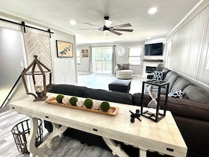 Un salon moderne avec un canapé, une table à manger agrémentée d’objets décoratifs, un ventilateur de plafond et une cheminée.