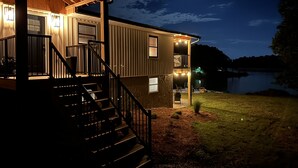 A two-story house with a wooden deck, a staircase, and a view of a lake at night. - STAY HERE! 2 Homes sleep up to 28! Private cove 2 docks and personal boat launch (Sevierville)