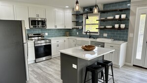 A modern kitchen with white cabinets, a stainless steel refrigerator, a built-in oven, a microwave, and a large island with stools. - STAY HERE! 2 Homes sleep up to 28! Private cove 2 docks and personal boat launch (Sevierville)