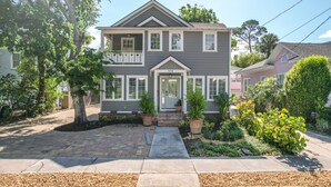 A two-story house with a front porch, a mailbox, and a small garden with potted plants.