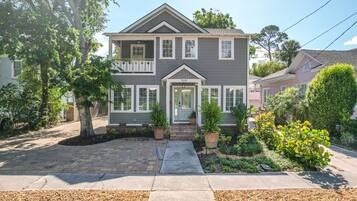 A two-story house with a front porch, a mailbox, and a small garden with potted plants.