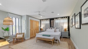A bedroom with a bed, a chair, a bedside table, a lamp, and a window with curtains.