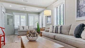 A living room with a beige sofa, a wooden coffee table with a bowl of decorative items, a red chair, and a ceiling fan.