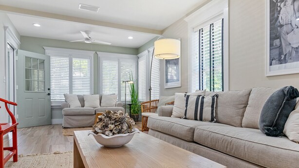 A living room with a beige sofa, a wooden coffee table with a bowl of decorative items, a red chair, and a ceiling fan.