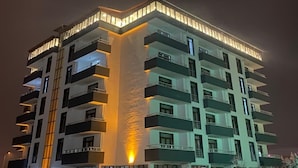 Un edificio de varios pisos con balcones, ventanas iluminadas y suelo cubierto de nieve.
