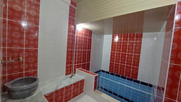 Une salle de bain avec des carreaux rouges et blancs formant un motif, un lavabo en marbre et une zone de douche carrelée de bleu.