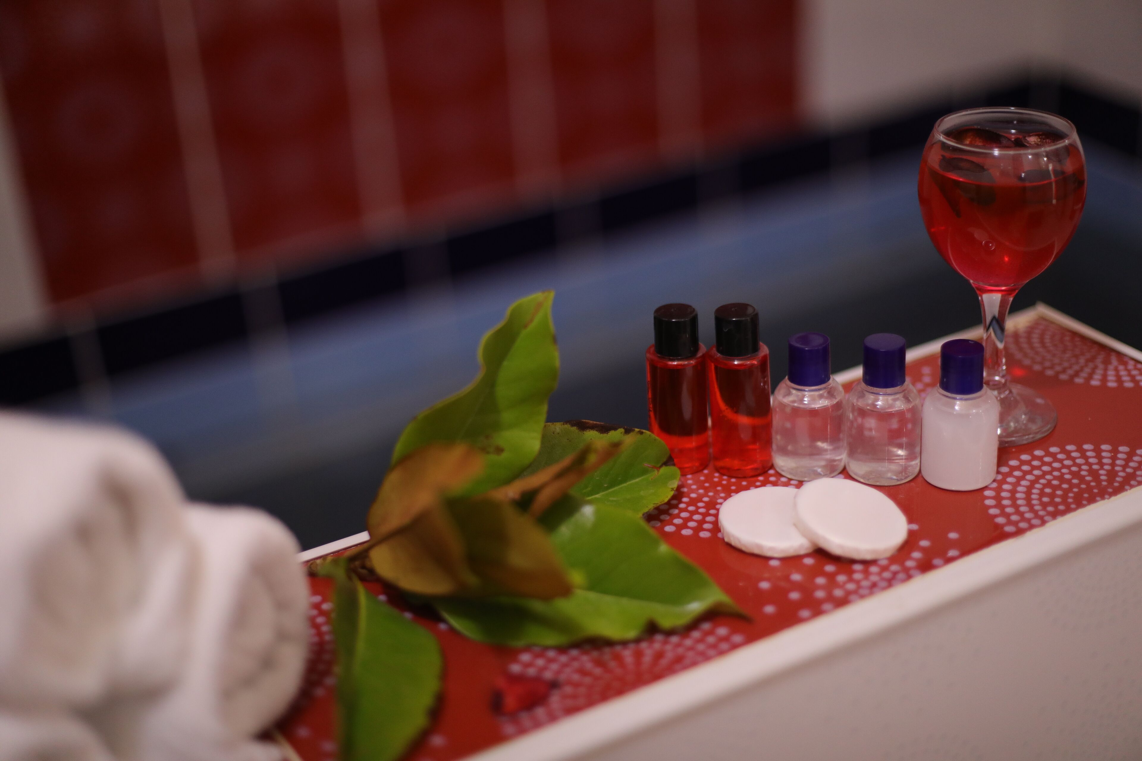 A tray with various toiletries and a glass of red liquid, likely a beverage, on a red and white patterned surface.