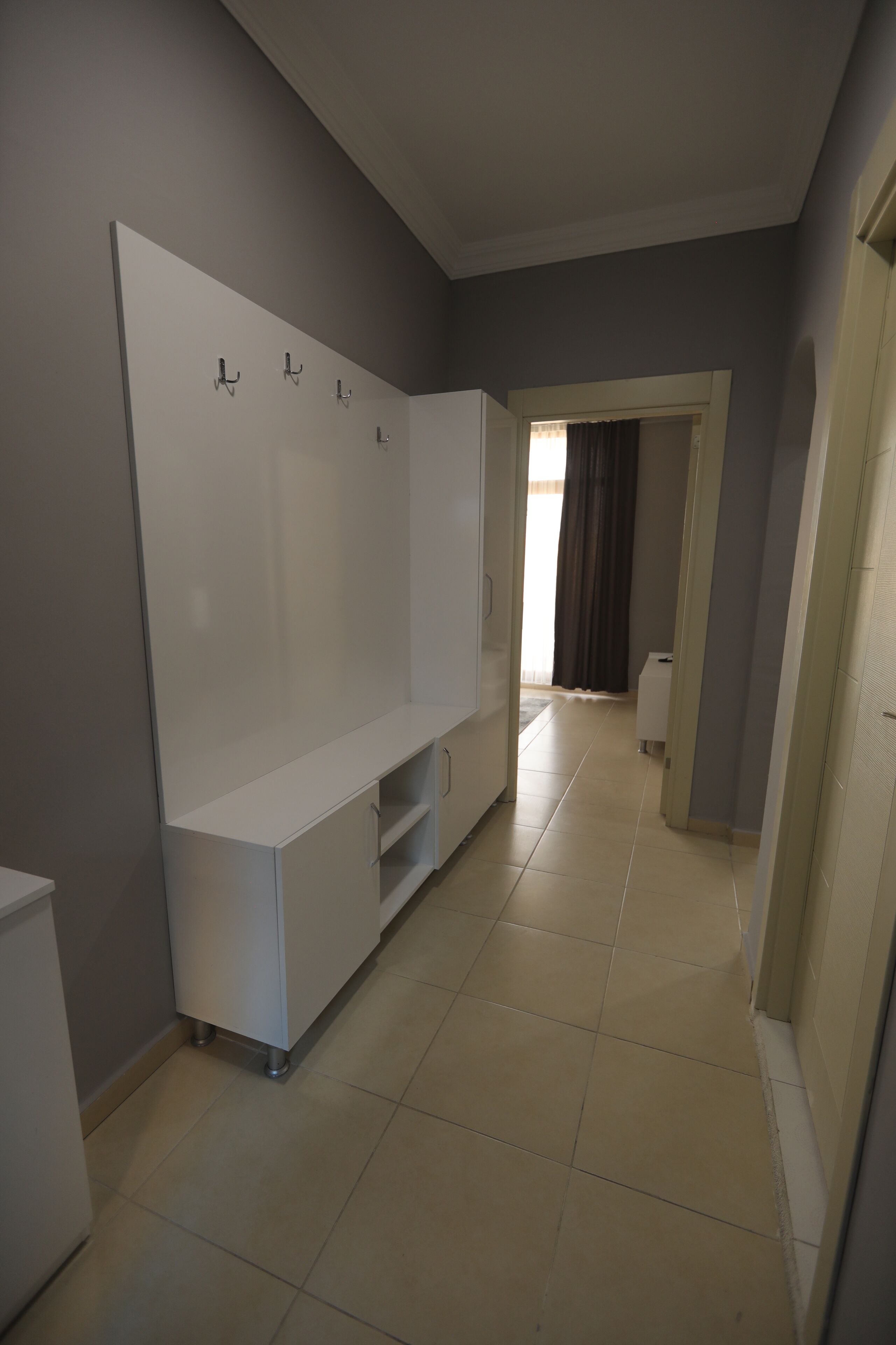 A room with a large white wardrobe, a small white cabinet, and a tiled floor.