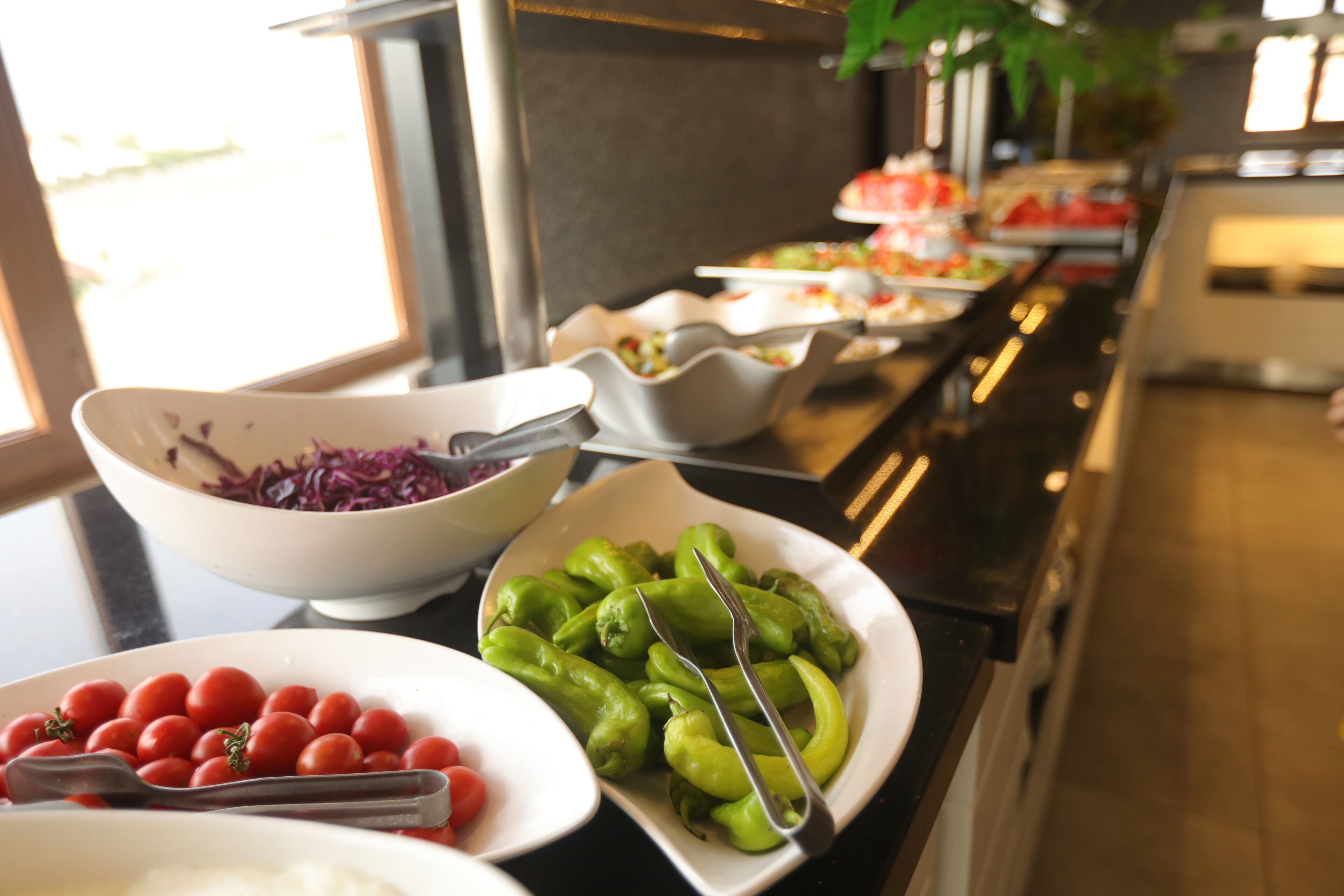 A buffet with various dishes including tomatoes, green peppers, and red cabbage.
