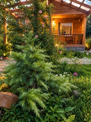 A wooden cabin with a porch, surrounded by a garden with various plants and flowers. - Family hotel Maia (Tsalka)