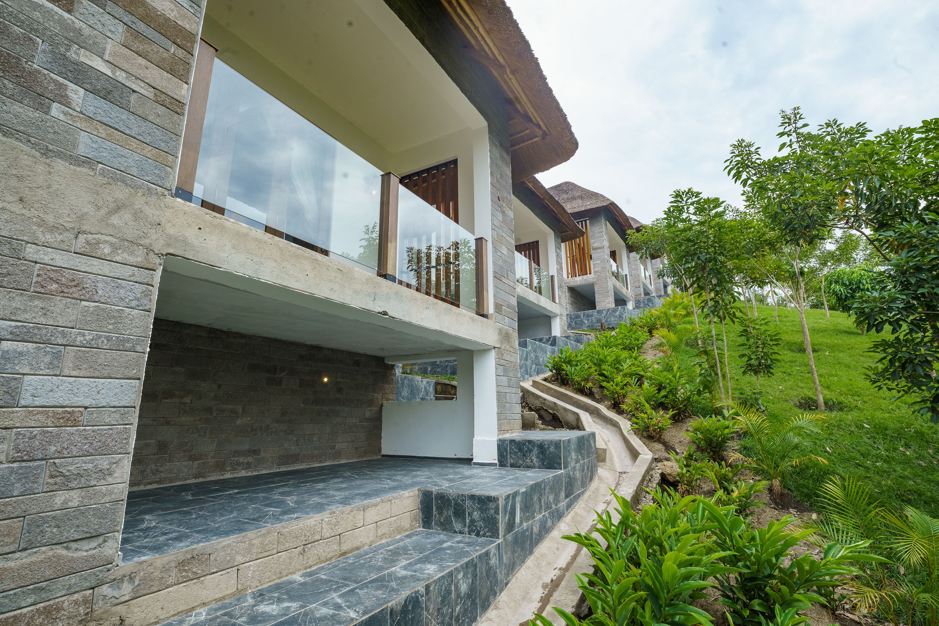 A modern building with a stone facade, a balcony with glass railings, and a landscaped garden area.