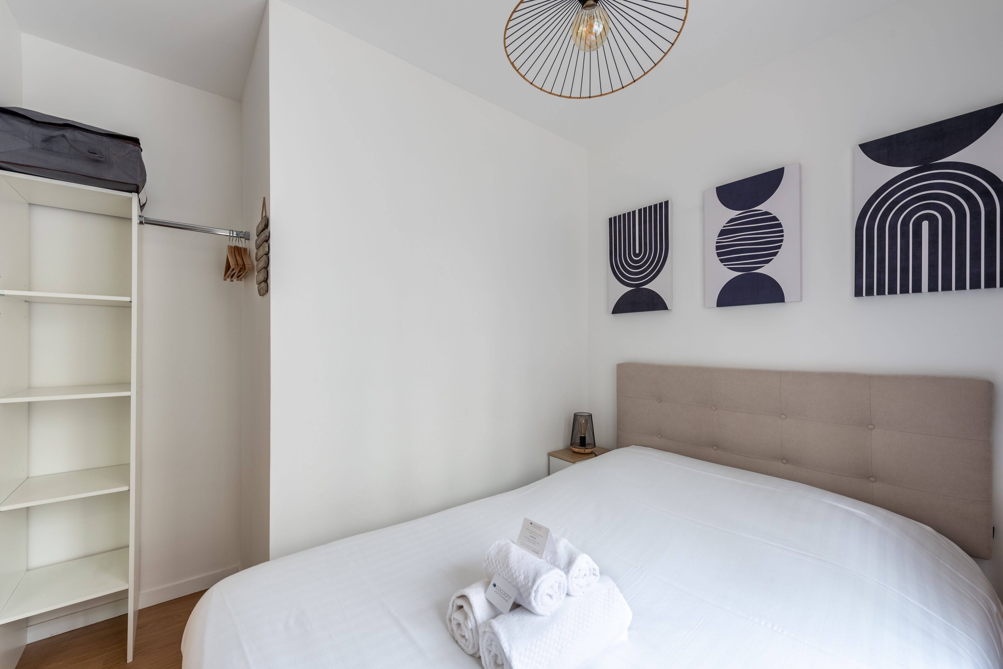 A neatly arranged bedroom with a bed, a wardrobe, and wall art.