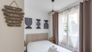 Ein Hotelzimmer mit Bett, Nachttisch, einer Hängelampe und Blick ins Freie durch ein Fenster mit Vorhängen.