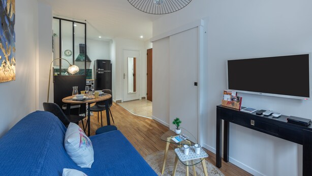 Ein modernes Wohnzimmer mit einem blauen Sofa, einem Glastisch und einem Flachbildfernseher auf einem schwarzen Lowboard.