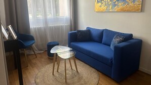 Ein Wohnzimmer mit einem blauen Sofa, einem Glastisch, einem blauen Sessel und einem Gemälde an der Wand.